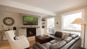 A living room with a fireplace, a sofa, a chair, and a television mounted above the fireplace.