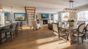 A spacious living room with a fireplace, a dining area with a large table and chairs, and a kitchen area with bar stools.