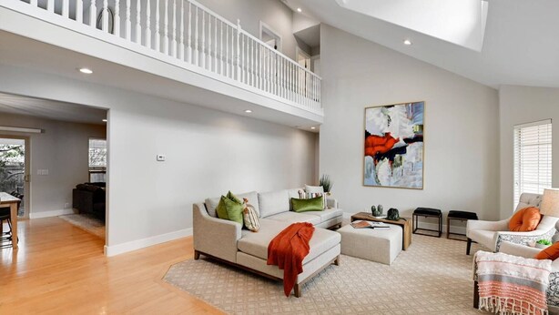 A spacious living room with a high ceiling and a balcony, featuring a sofa, a coffee table, and a painting on the wall. - Modern Salt Lake City Retreat: Spacious 5BR Home, Game Room, BBQ, Free Ski Rental, Covered Patio (Salt Lake City)