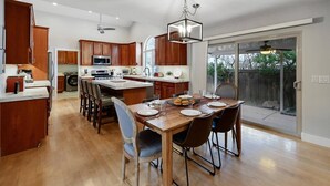 A spacious kitchen with wooden cabinets, a large island, and a dining area with a table set for four. - Modern Salt Lake City Retreat: Spacious 5BR Home, Game Room, BBQ, Free Ski Rental, Covered Patio (Salt Lake City)
