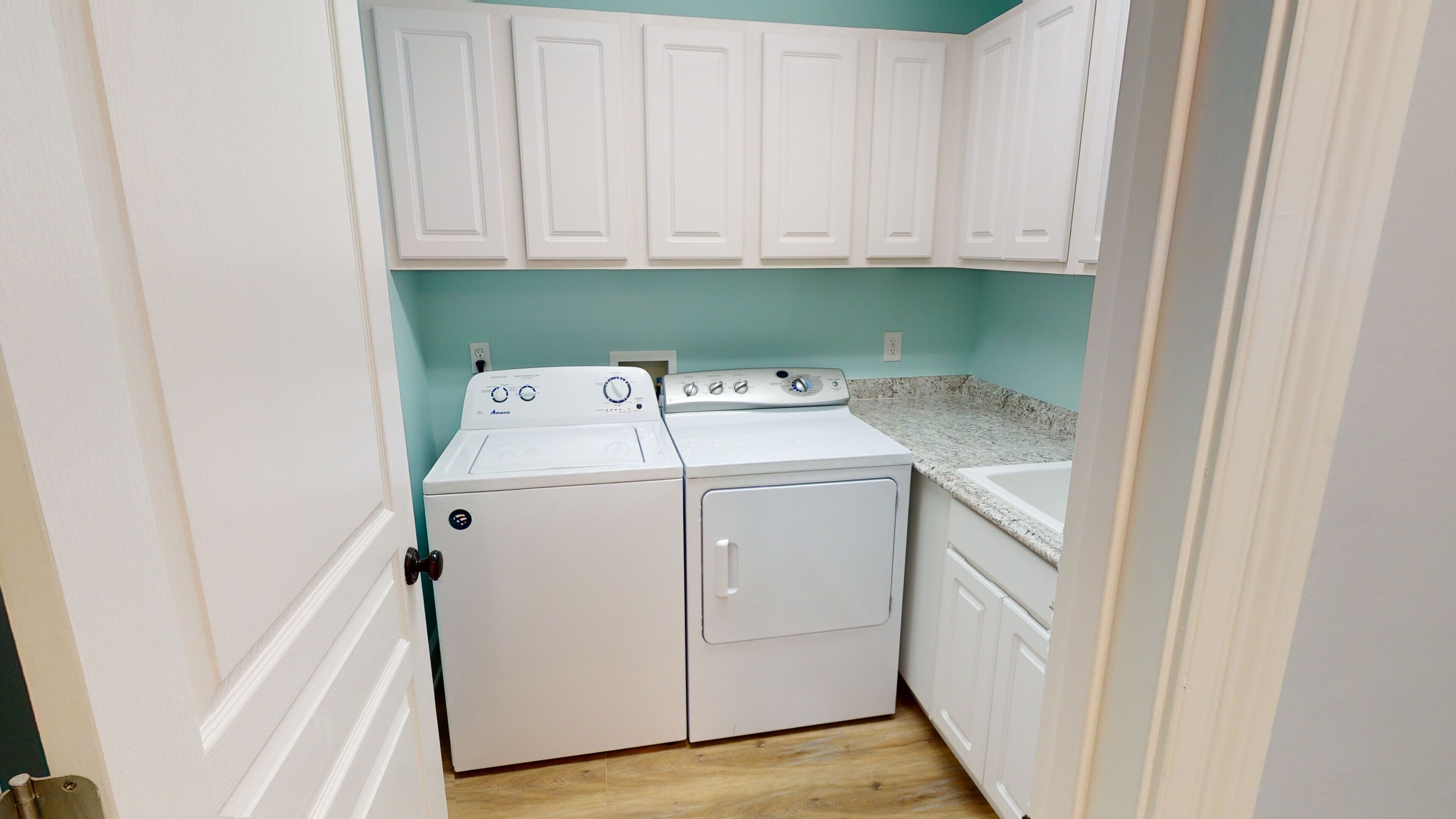 A laundry room with a washer and dryer, cabinets above, and a countertop with a sink.