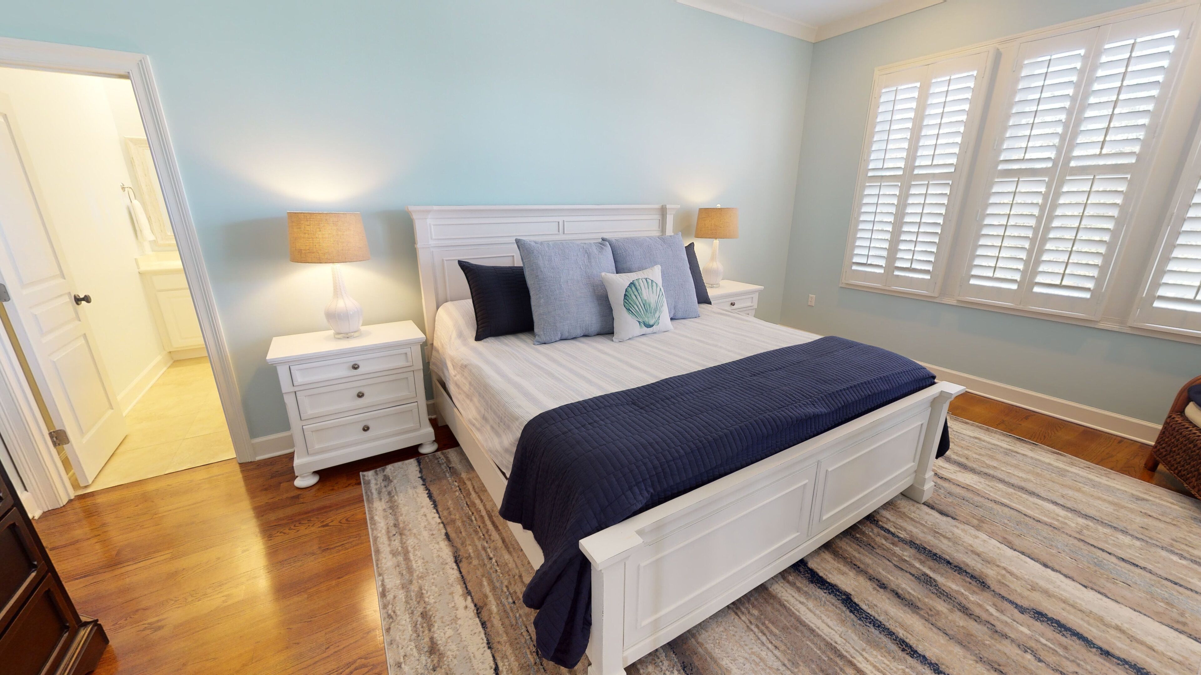 A bedroom with a bed, nightstands, a lamp, and a window with shutters.