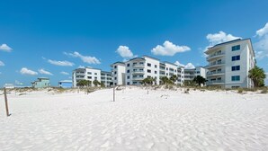 Ett hotell vid stranden med flera våningar, en sandstrand i förgrunden och en klarblå himmel.