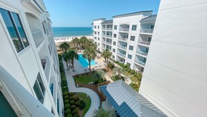 Ett högt hotell med en swimmingpool, palmer och utsikt över stranden.