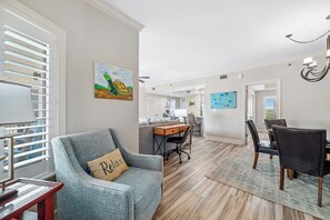 Un salon spacieux avec un fauteuil gris, un bureau en bois et un coin repas avec des chaises.