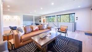 Een moderne woonkamer met een leren bank, een houten salontafel, en een eethoek met een bankje en stoelen.