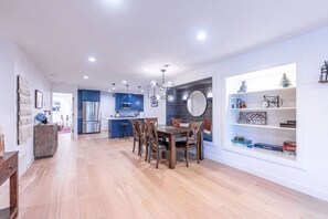 Une cuisine moderne avec des meubles bleus, un coin repas avec une table et des chaises en bois, et une bibliothèque contenant divers objets.