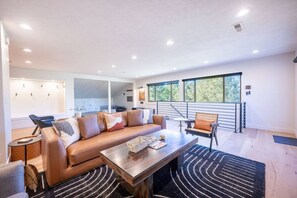 Un salon moderne avec un canapé, une table basse et une vue sur l’extérieur grâce à de grandes fenêtres.