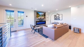 Een ruime woonkamer met een open haard, een bank, een televisie en een balkon met een hekwerk.