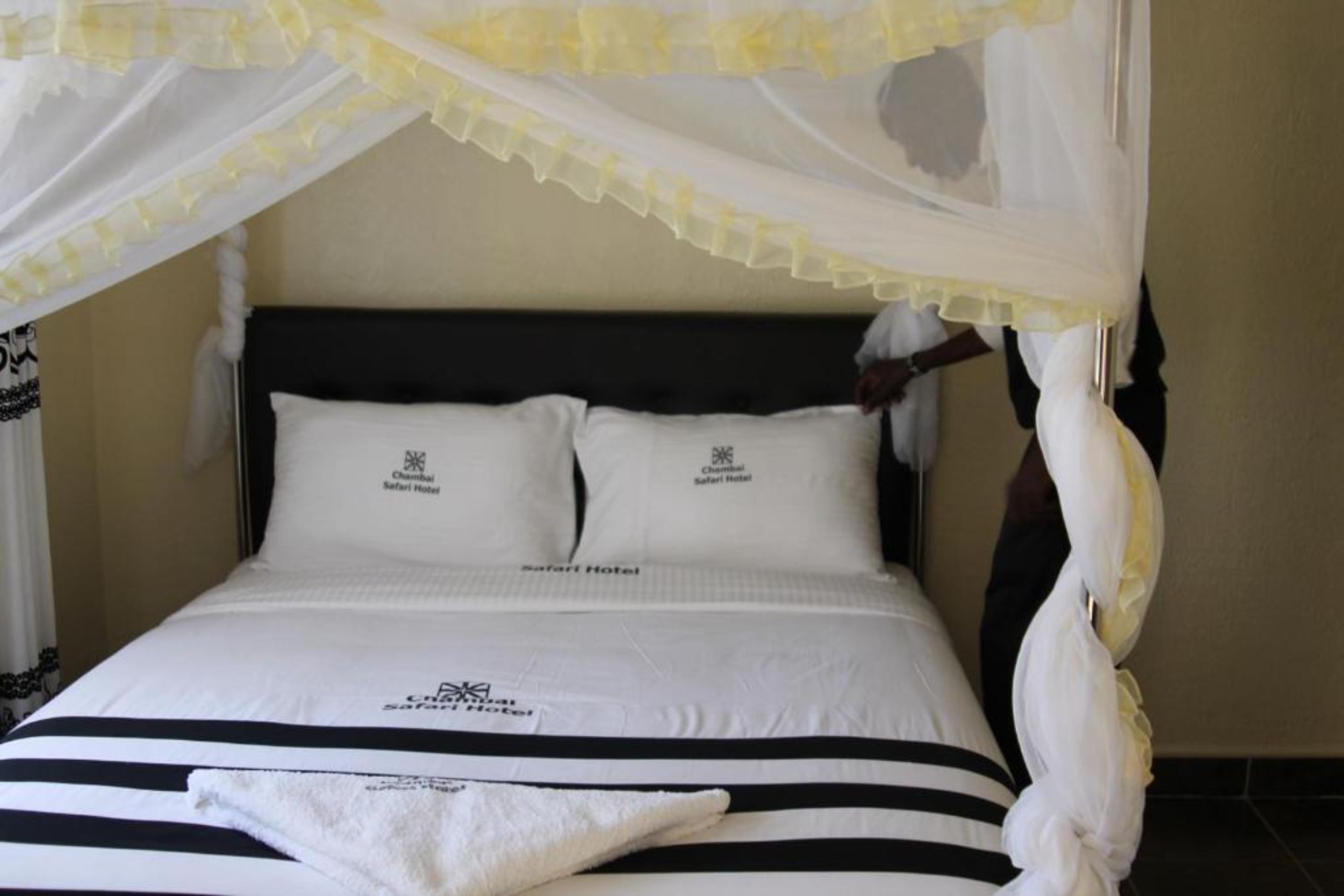 Un letto a baldacchino, due cuscini e una coperta con il logo dell'Hotel Safari.