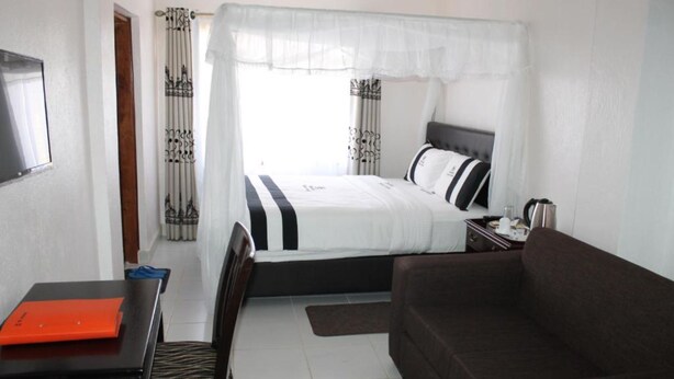A bedroom with a bed, a desk, a chair, a sofa, and a window with curtains. - Chambai Safari Hotel (Naivasha)