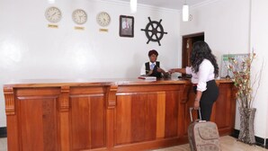 A reception desk with clocks indicating different time zones, a ship's wheel, and a framed picture on the wall. - Chambai Safari Hotel (Naivasha)