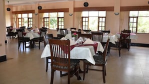 A dining area with multiple tables and chairs, large windows, and a tiled floor. - Chambai Safari Hotel (Naivasha)