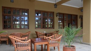 A covered patio area with wicker furniture and large windows. - Chambai Safari Hotel (Naivasha)