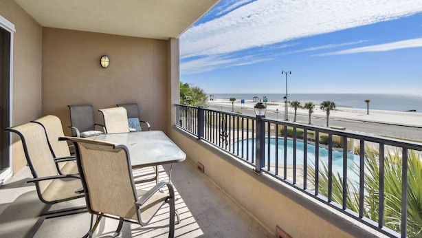 Un balcón con mesa y sillas, una piscina y vistas a la playa y al océano.