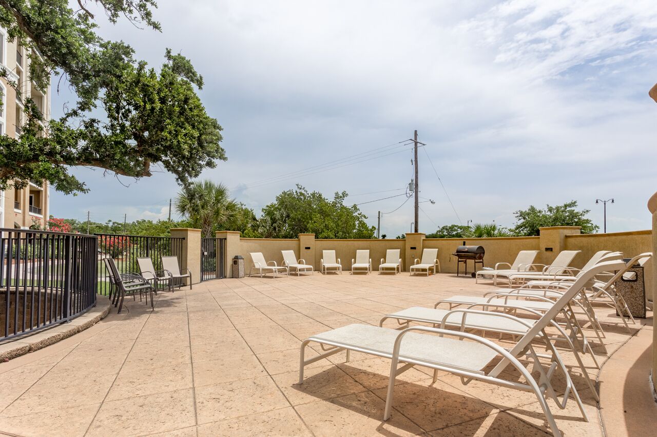 Un patio al aire libre con tumbonas, una parrilla y vistas a un edificio con un árbol.