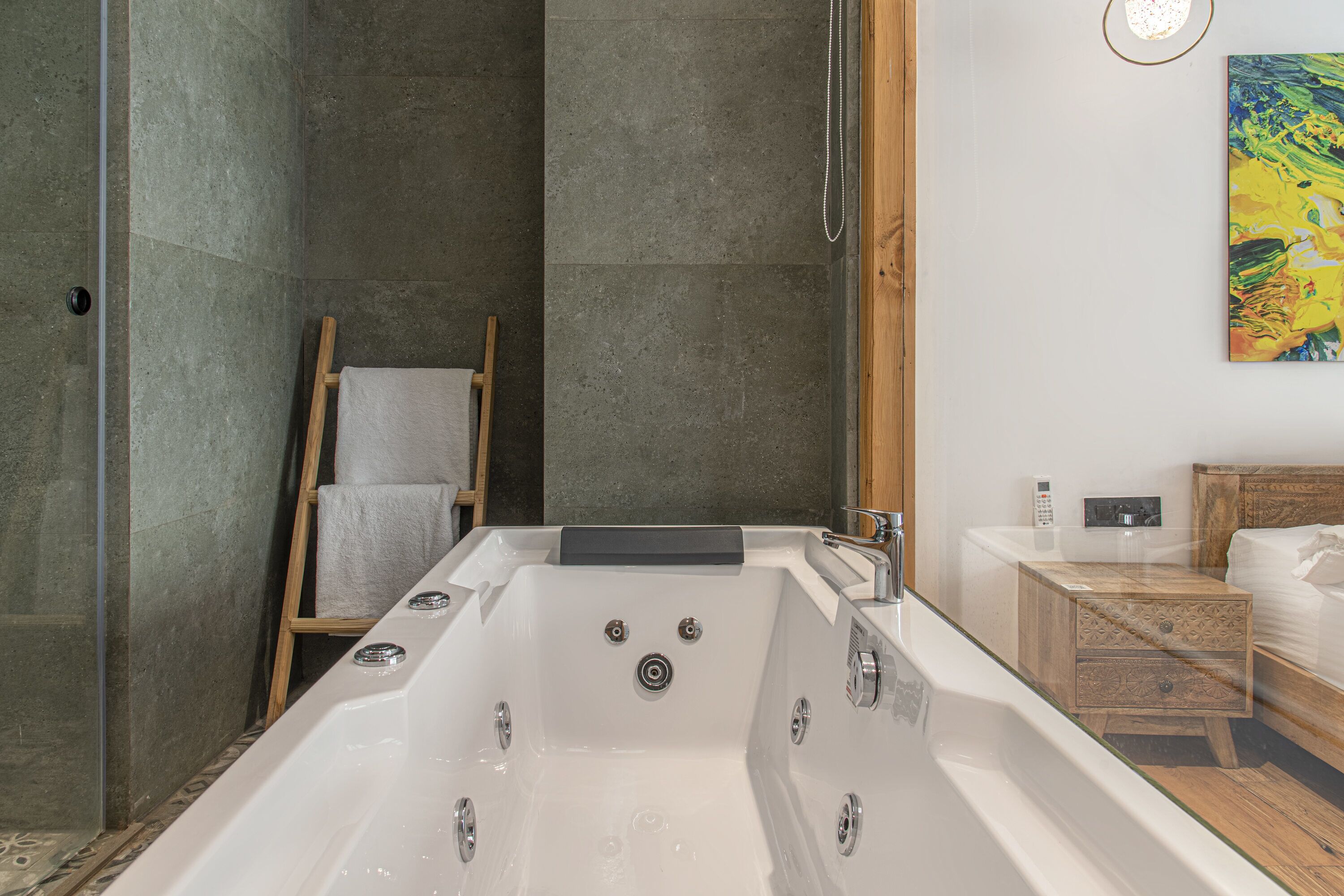 A modern bathroom with a large bathtub, a wooden ladder, a wooden nightstand, and a painting on the wall.