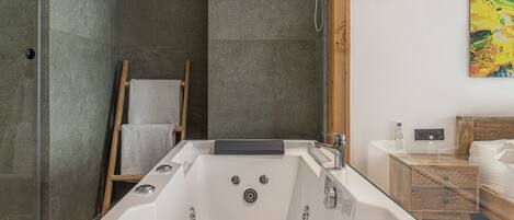 A modern bathroom with a large bathtub, a wooden ladder, a wooden nightstand, and a painting on the wall.