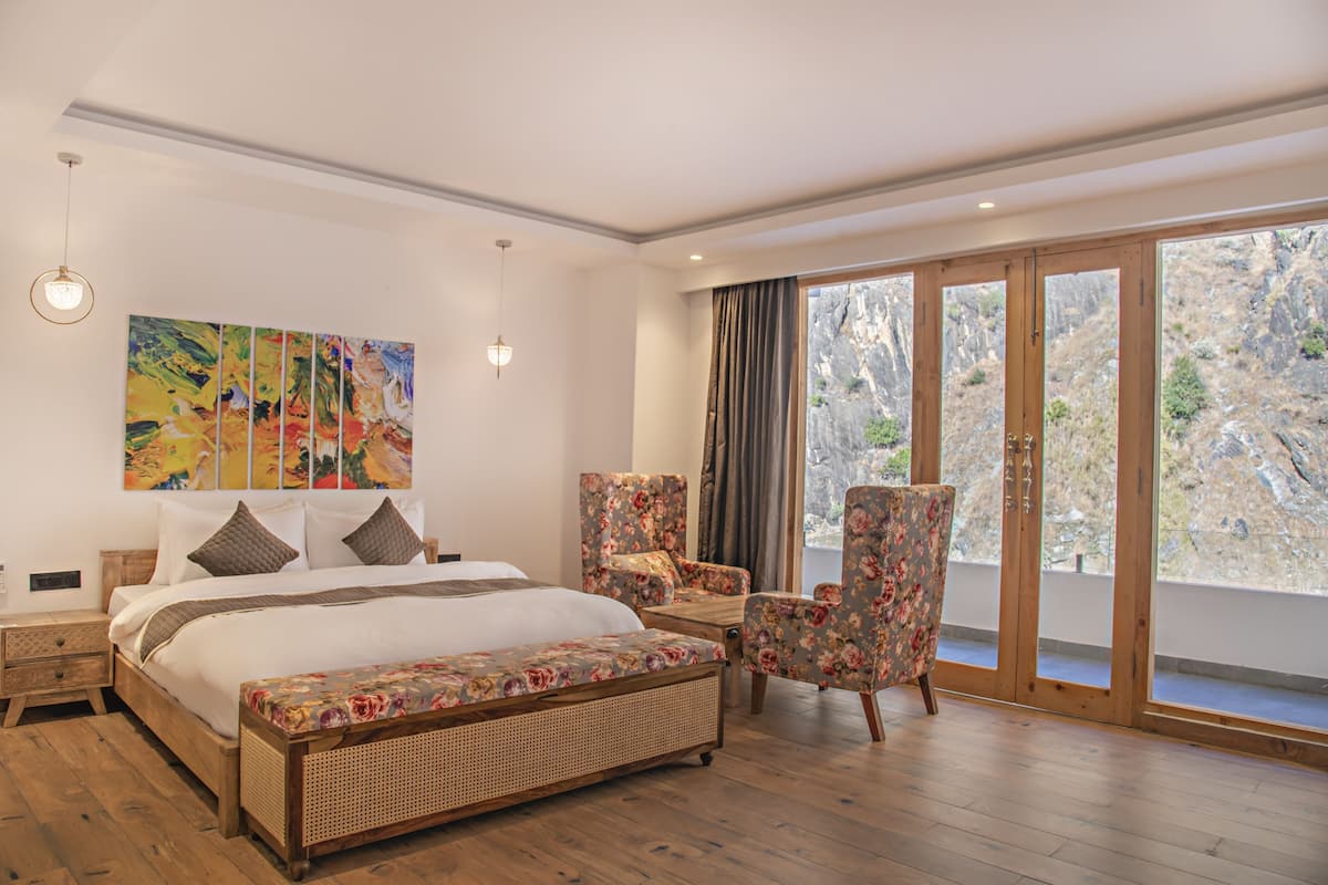 Quarto com uma cama grande, uma cadeira, um banco, um quadro e vista através de uma porta de vidro.