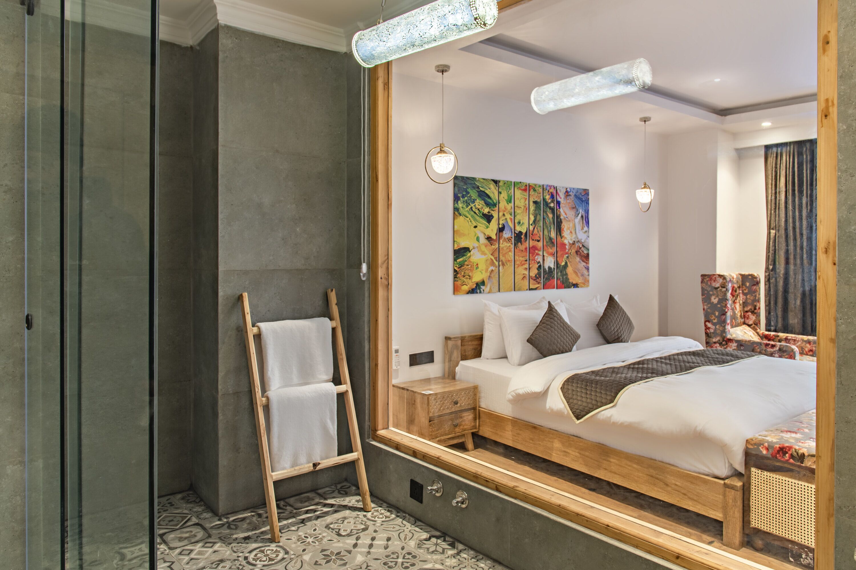 Una habitación de hotel moderna con una cama grande, una escalera de madera, una mesita de noche y un cuadro abstracto colorido en la pared.