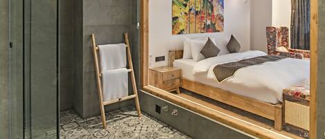 A modern hotel room with a large bed, a wooden ladder, a nightstand, and a colorful abstract painting on the wall.