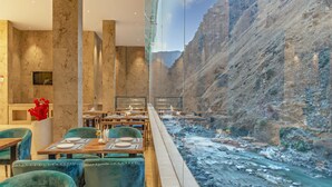 A restaurant with a view of a river canyon, featuring marble walls, green velvet chairs, and wooden tables. - Echor Palm Bliss Riverside Resort & Spa Kasol (Bhuntar)