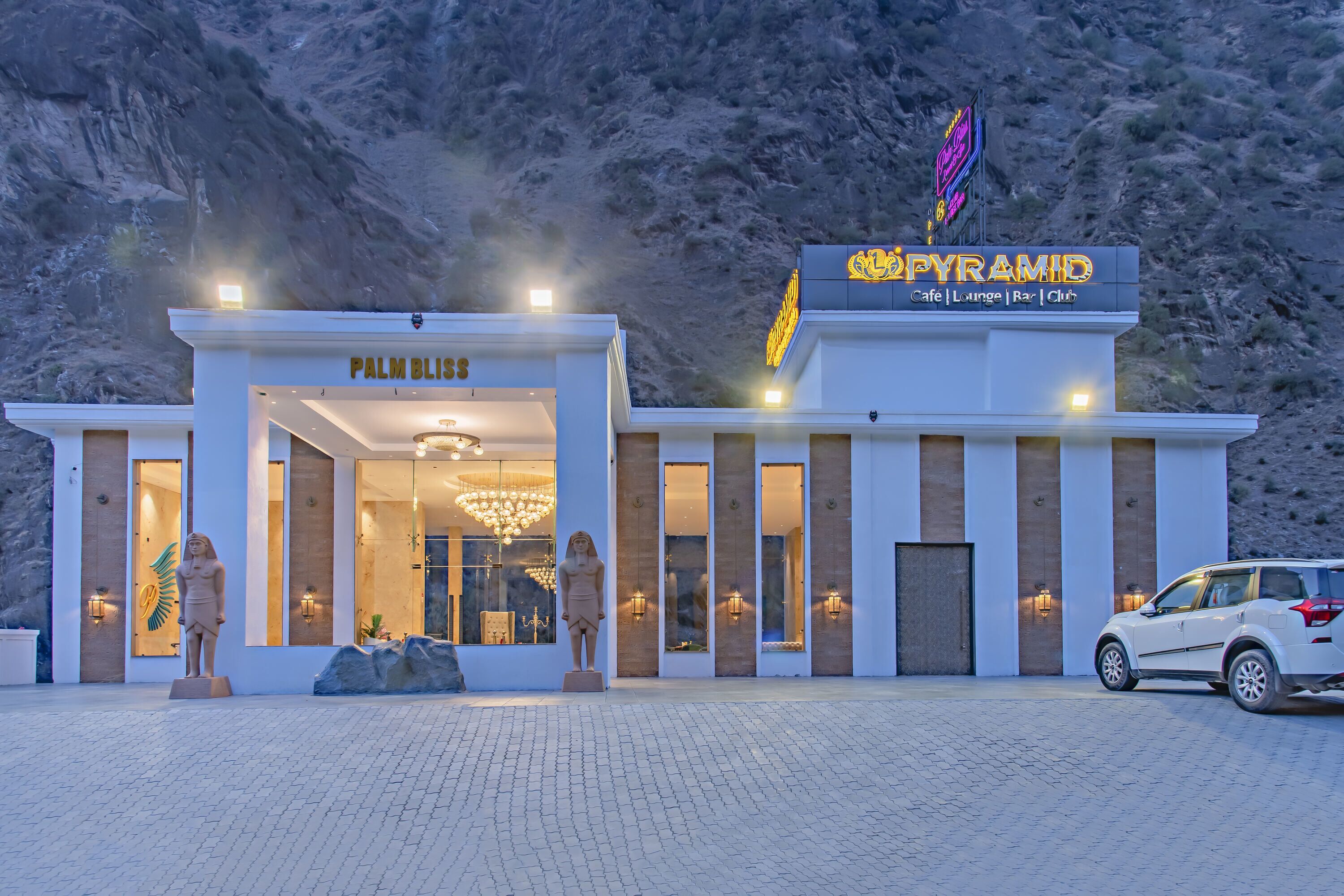 A modern building with a sign reading "PYRAMID" and "PALM BLISS" indicating a hotel or resort.