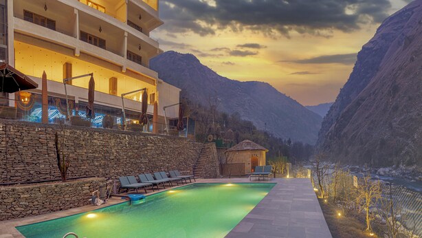 A swimming pool with lounge chairs, a spa building, and a mountain backdrop. - Echor Palm Bliss Riverside Resort & Spa Kasol (Bhuntar)