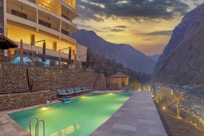 A swimming pool with lounge chairs, a spa building, and a mountain backdrop. - Echor Palm Bliss Riverside Resort & Spa Kasol (Bhuntar)