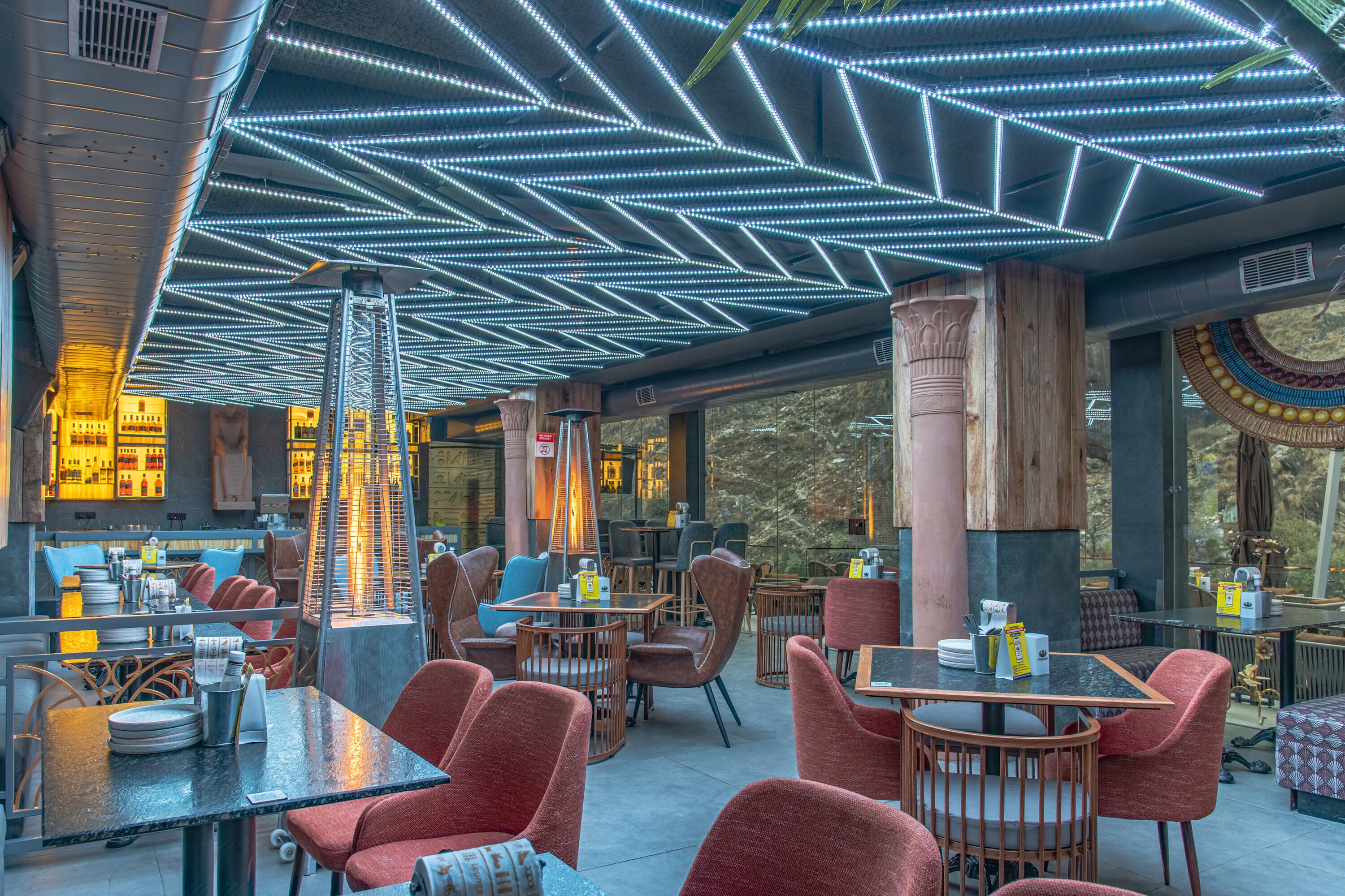 Ein Restaurant mit moderner Einrichtung, ausgestattet mit einer Decke mit linearen LED-Leuchten, Holzsäulen und unterschiedlichen Sitzgelegenheiten.