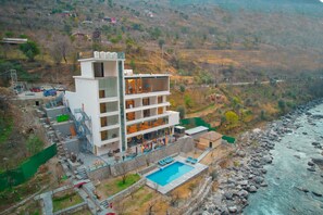 Un hotel de varios pisos con piscina, situado cerca de una orilla rocosa de río.