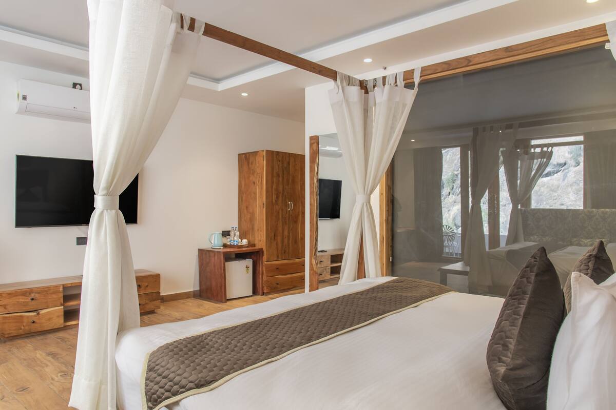 Quarto com cama, guarda-roupa de madeira, televisão e janela com cortinas.