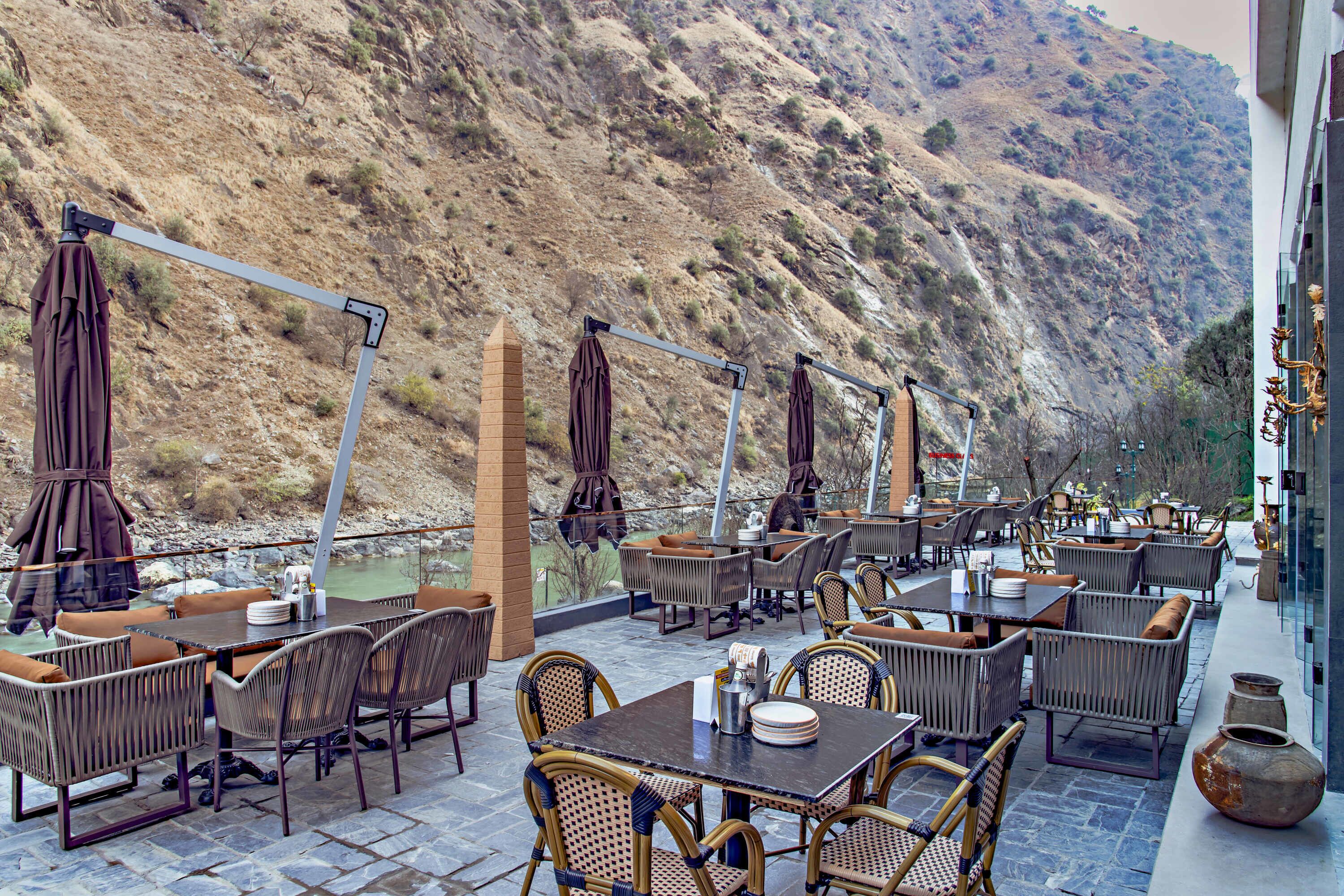 An outdoor patio with wicker furniture, tables, and chairs, overlooking a mountainous landscape.