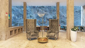 A lobby with two armchairs, a chandelier, a dining area, and a large window with a view of trees. - Echor Palm Bliss Riverside Resort & Spa Kasol (Bhuntar)