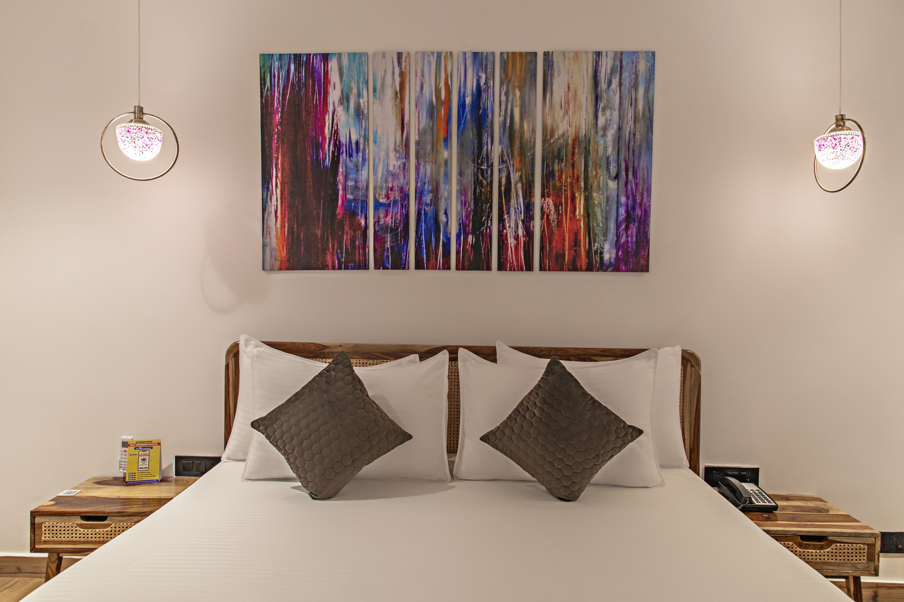 A hotel room with a large bed, two nightstands, a painting on the wall, and two pendant lights.