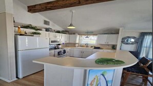 A kitchen with white cabinets, a white refrigerator, a wooden ceiling beam, and a dining area with a table and chairs. - Cozy and Clean steps from the beach. Gulf views <3 (Freeport)