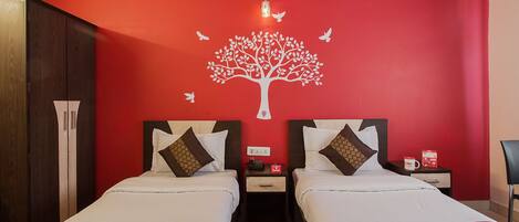 Habitación de hotel con dos camas, una pared roja con un mural de un árbol blanco y una mesita de noche con un teléfono y una caja roja.