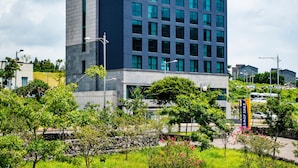 Um edifício moderno com fachada de vidro e concreto, cercado por grama verde e pequenas árvores.