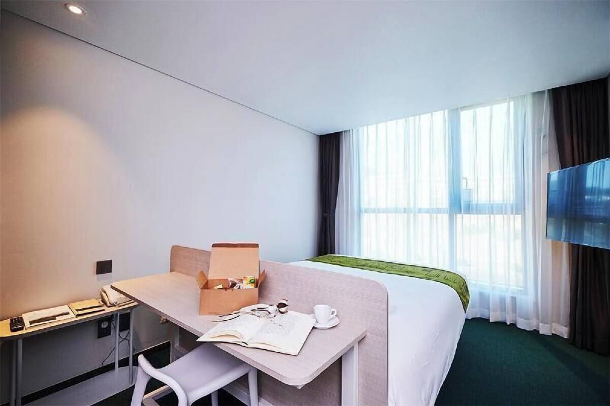 Une chambre d’hôtel comprenant un lit, un bureau avec une chaise, une télévision et une fenêtre avec des rideaux.