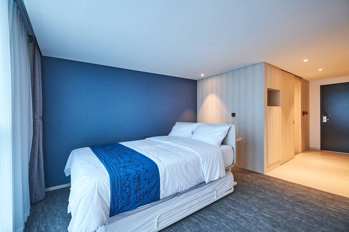 Une chambre d’hôtel moderne avec un grand lit, un mur d’accent bleu et une armoire en bois.