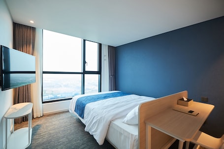 Habitación de hotel con cama, escritorio, televisión montada en la pared y un ventanal con vistas.