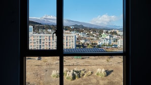 Vista pela janela de um horizonte urbano com edifícios, uma montanha e céu claro.