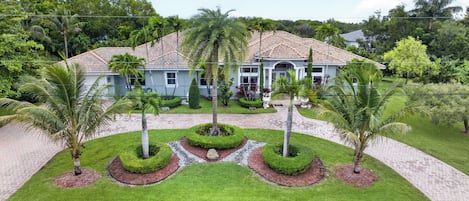 A two-story house with a tiled roof, surrounded by a well-maintained lawn and palm trees.