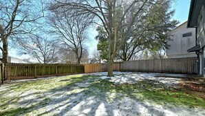 A backyard with a wooden fence, a tree, and a building in the background. - Modern Pflugerville Home Near Austin and Tech Hub (Pflugerville)
