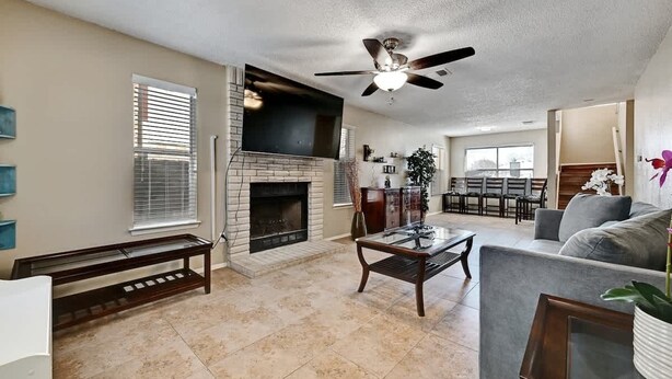 A living room with a fireplace, a ceiling fan, and a dining area in the background. - Modern Pflugerville Home Near Austin and Tech Hub (Pflugerville)