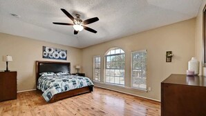 A bedroom with a bed, wooden flooring, a ceiling fan, and large windows with blinds. - Modern Pflugerville Home Near Austin and Tech Hub (Pflugerville)