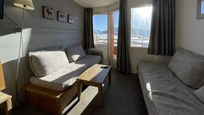 Ein gemütliches Zimmer mit einer Couch, einer Holzbank und einer Lampe. An der Wand hängen drei gerahmte Bilder.