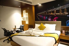 A hotel room with a bed, a desk, a chair, and a wall-mounted TV displaying a cityscape. - Namo Residency (Vijayawada)