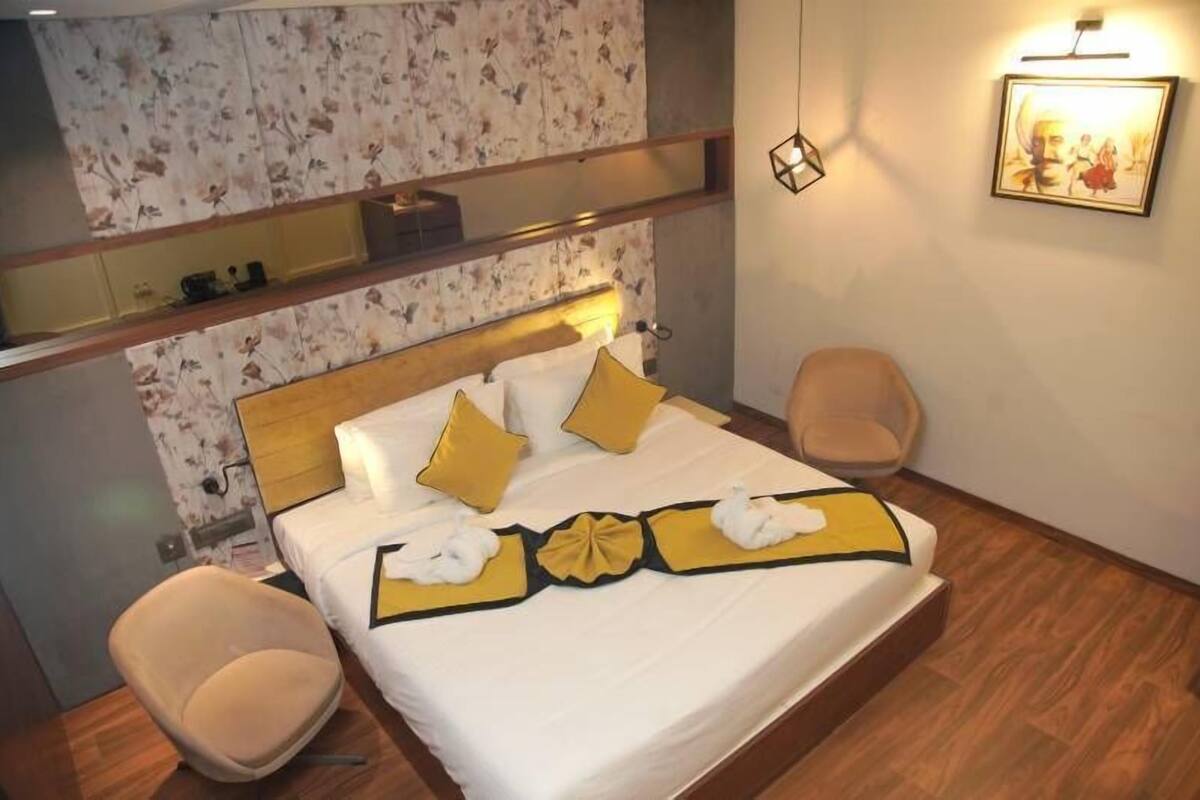 A hotel room with a bed, a chair, a mirror, and a wall-mounted picture.