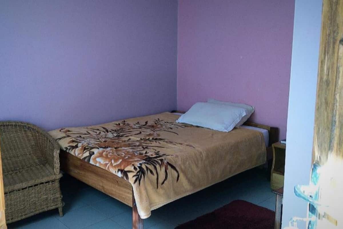 A small bedroom with a single bed, a wicker chair, and a wooden door.
